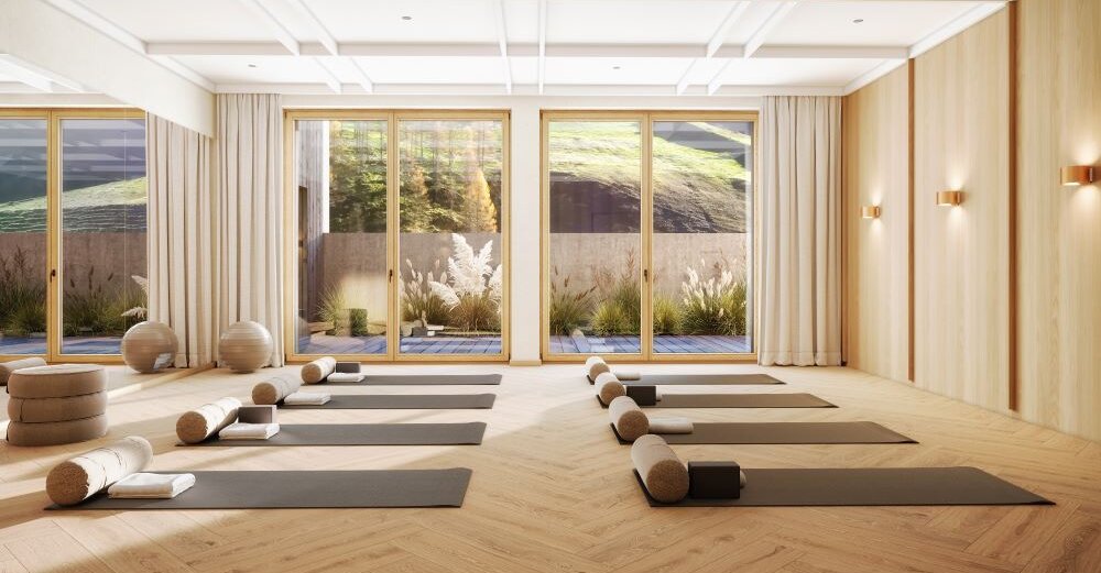 Ein heller Yogaraum mit Holzfußboden, ausgestattet mit Matten und Kissen, bietet eine ruhige Atmosphäre für Entspannung.