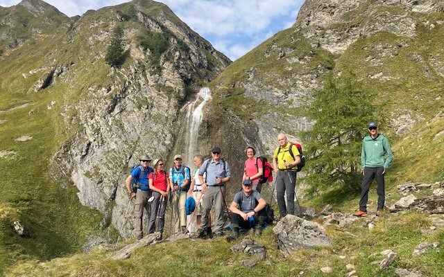 Eine Gruppe von Wanderern posiert vor einer beeindruckenden Berglandschaft mit einem Wasserfall im Hintergrund.