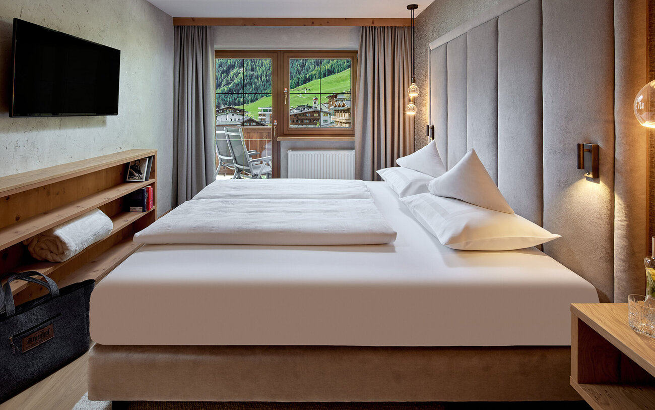 Ein modernes Schlafzimmer mit einem großen Bett, sanften Farben und einem Fenster, das auf eine grüne Berglandschaft blickt.