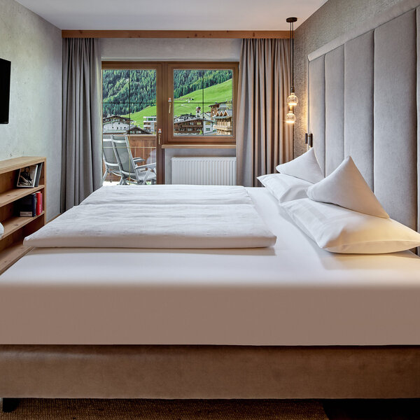 Ein modernes Schlafzimmer mit einem großen Bett, sanften Farben und einem Fenster, das auf eine grüne Berglandschaft blickt.