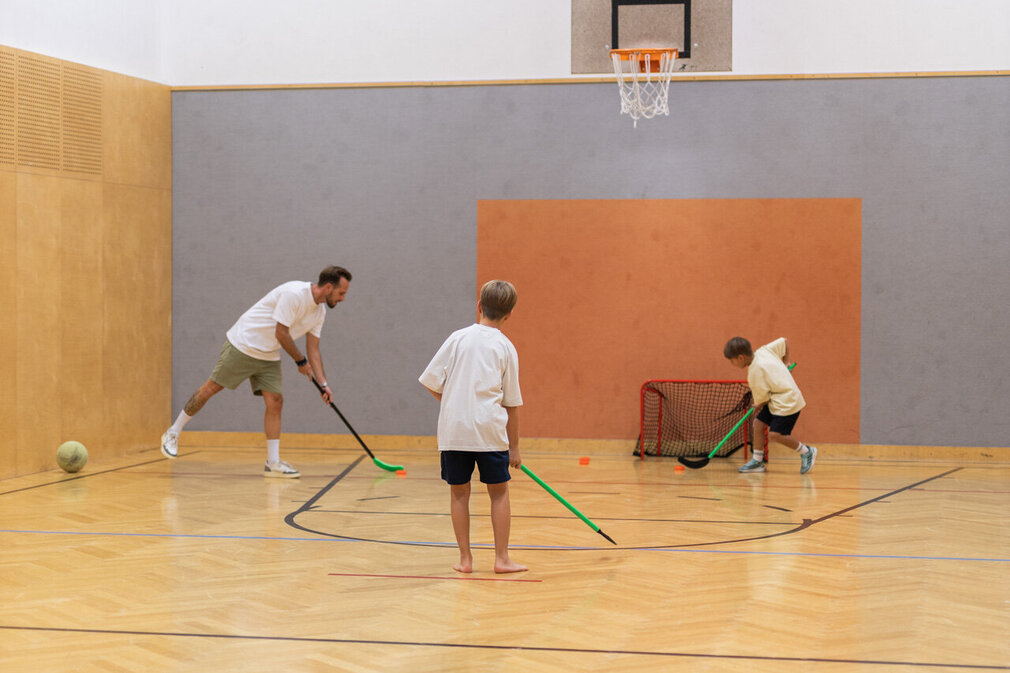 Ein Mann und zwei Kinder spielen Hockey in einem Turnsaal.