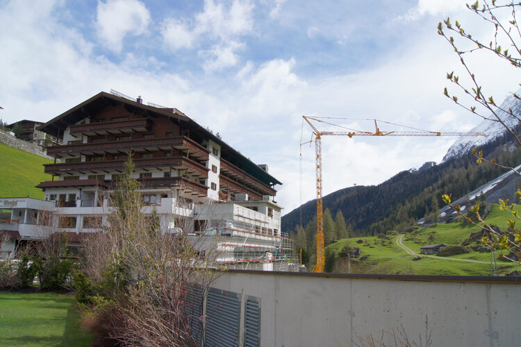 Das Bild zeigt ein mehrstöckiges Hotelgebäude, umgeben von Bergen und einem Baukran, der an einem neuen Projekt arbeitet.