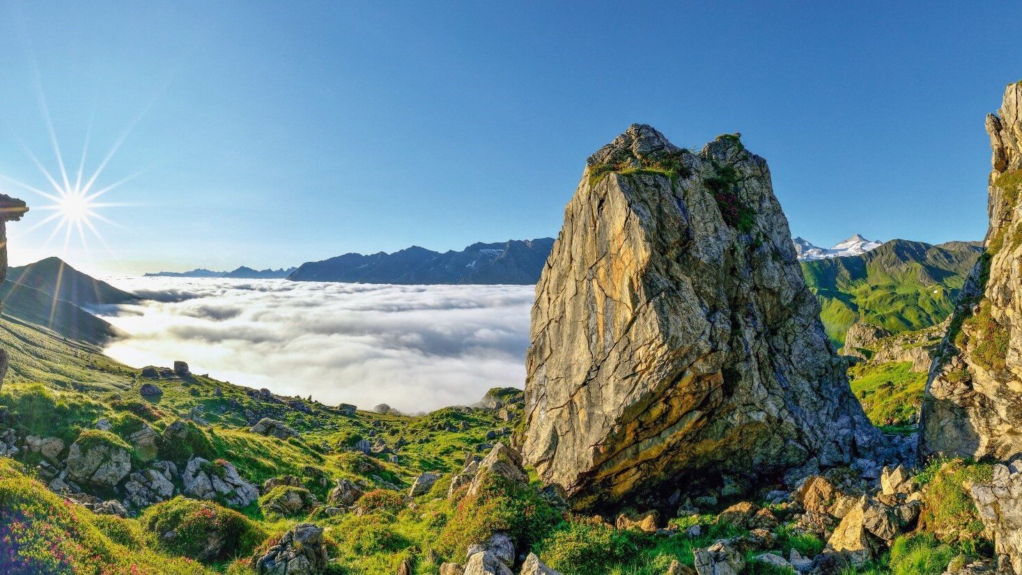 Ein atemberaubender Blick auf die Berge, umgeben von Wolken, während die Sonne strahlend am Himmel steht.