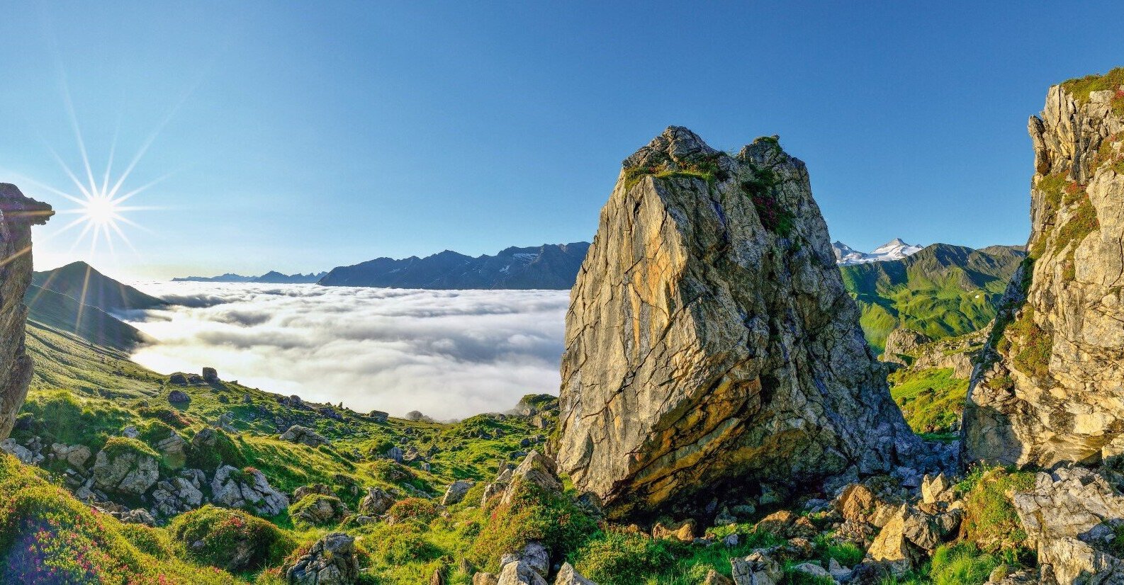 Ein atemberaubender Blick auf die Berge, umgeben von Wolken, während die Sonne strahlend am Himmel steht.