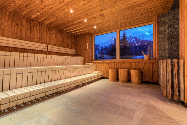 Ein gemütlicher Saunaraum mit Holzverkleidung, Bänken und Blick auf die Berge bei Dämmerung.