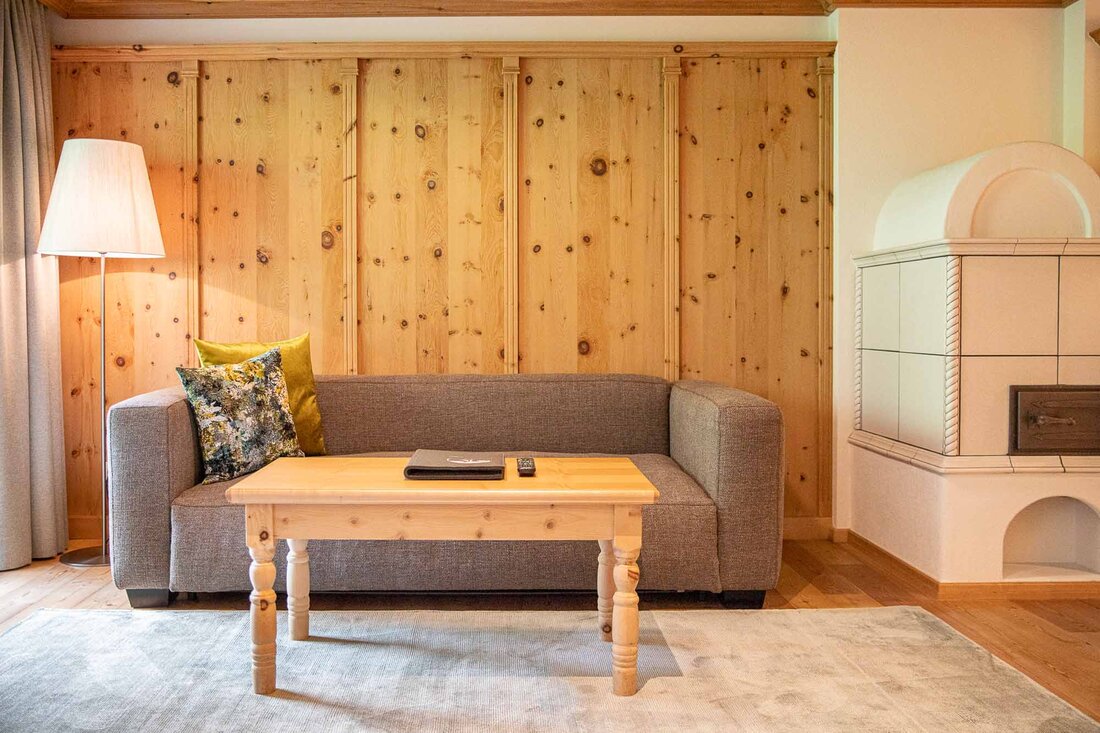 Ein gemütliches Wohnzimmer mit einer grauen Couch, einem Holztisch und einer Stehlampe vor einer Holzvertäfelung.