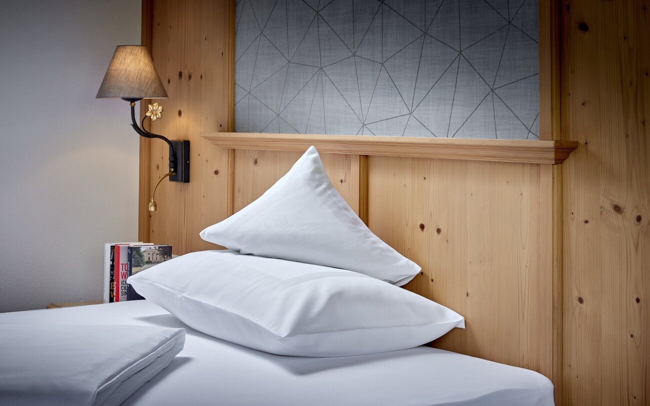 Ein gemütliches Schlafzimmer mit einem Holzpaneel, einem eleganten Nachttisch und zwei weißen Kissen auf dem Bett.