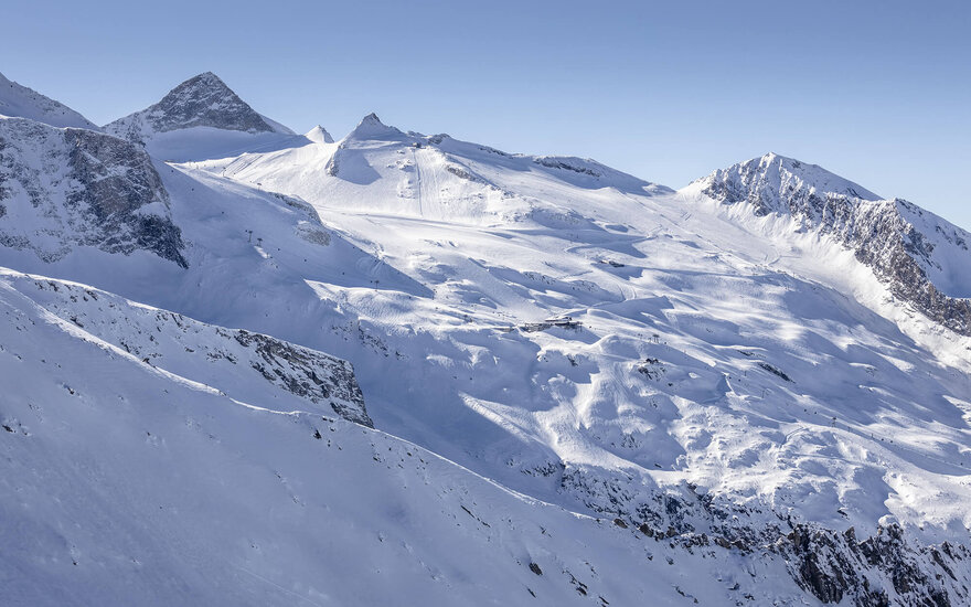 Eine beeindruckende Berglandschaft mit schneebedeckten Gipfeln und sanften Hängen unter einem klaren blauen Himmel.