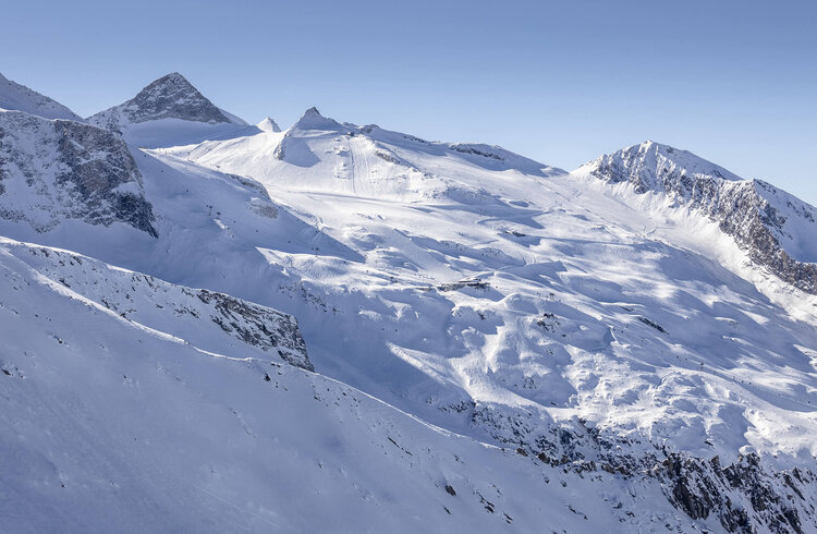 Eine beeindruckende Berglandschaft mit schneebedeckten Gipfeln und sanften Hängen unter einem klaren blauen Himmel.