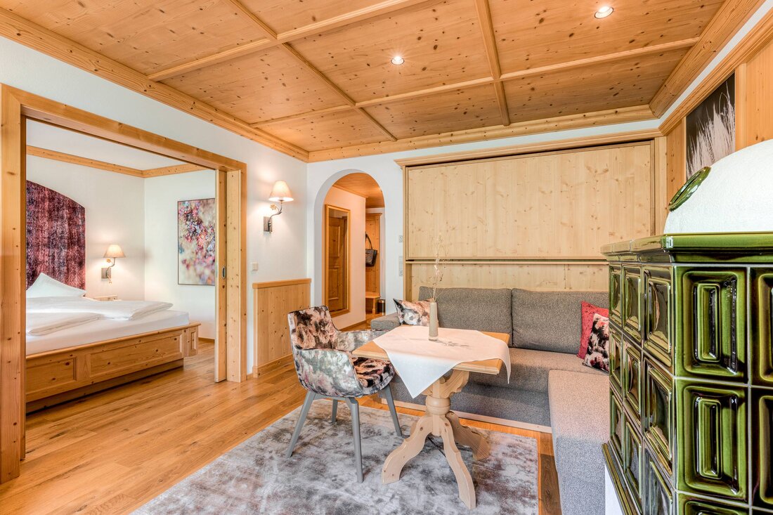 Ein gemütliches Wohnzimmer mit einem Holztisch, einem grauen Sofa und einem dekorativen Ofen in einem modernen alpinen Stil.