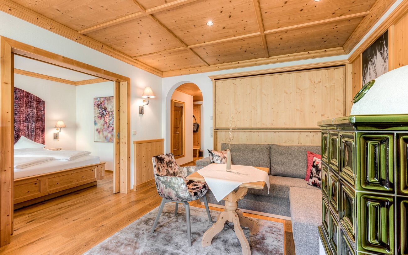 Ein gemütliches Wohnzimmer mit einem Holztisch, einem grauen Sofa und einem dekorativen Ofen in einem modernen alpinen Stil.