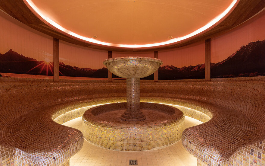 Ein eleganter Dampfbadbereich mit einem zentralen, mosaikverzierten Brunnen und sanfter, warmen Beleuchtung.