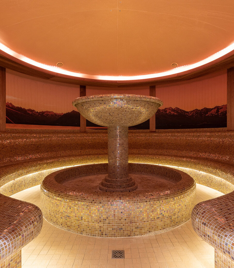 Ein eleganter Dampfbadbereich mit einem zentralen, mosaikverzierten Brunnen und sanfter, warmen Beleuchtung.