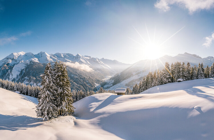 Eine atemberaubende Winterlandschaft mit schneebedeckten Bergen und strahlender Sonne, die den Himmel erleuchtet.
