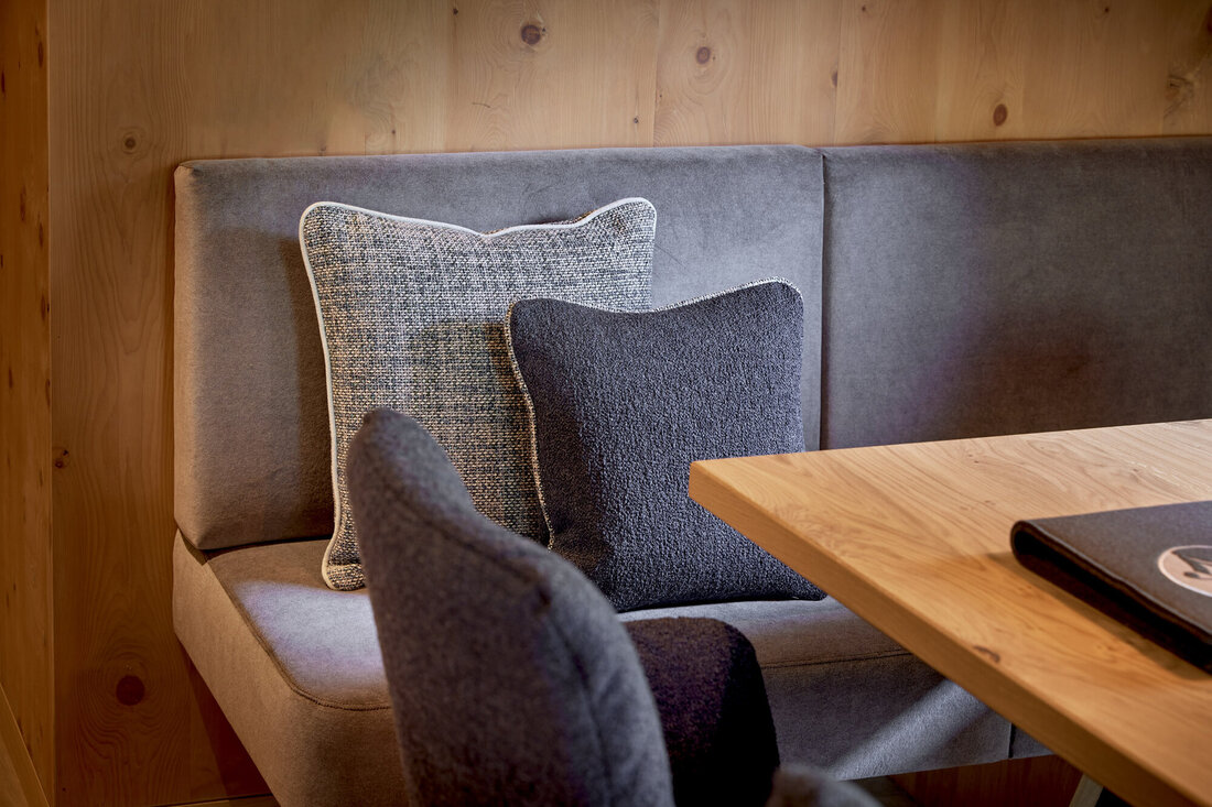 Eine gemütliche Sitzecke mit grauen Kissen und einem Holzstammtisch, umgeben von warmen Holzwänden.