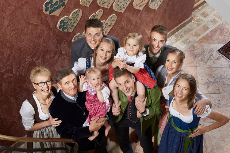 Eine fröhliche Familie posiert auf einer Treppe, gekleidet in traditionelle Trachten, umgeben von herzförmigen Bildern.
