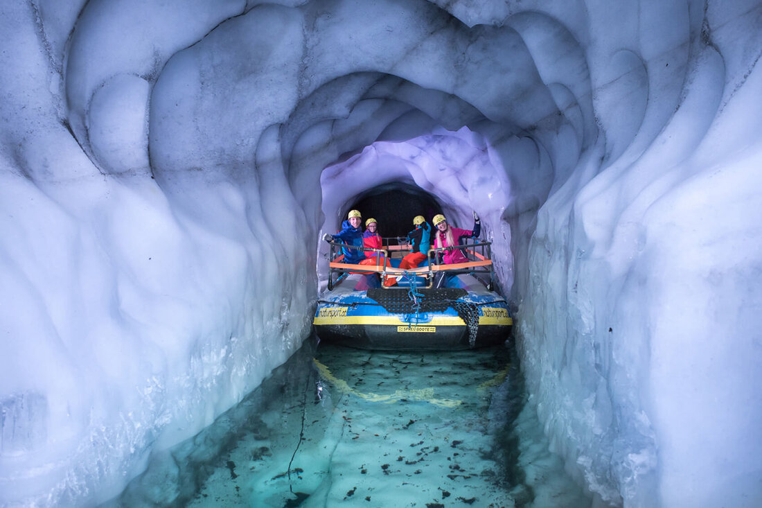 Eine Gruppe von vier Personen in bunten Anzügen sitzt in einem Boot, das durch einen eisigen Tunnel fährt.