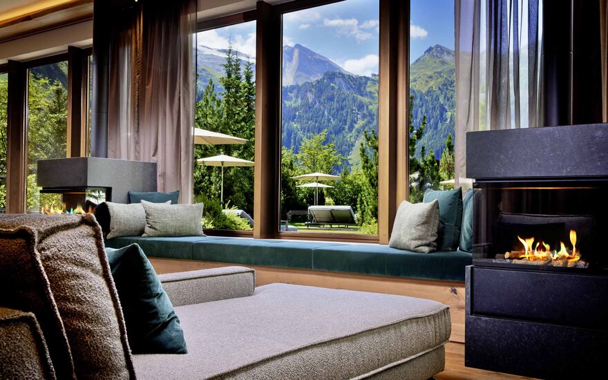 Ein gemütlicher Wohnraum mit einem modernen Kamin und Blick auf die majestätischen Berge und üppige Bäume im Freien.