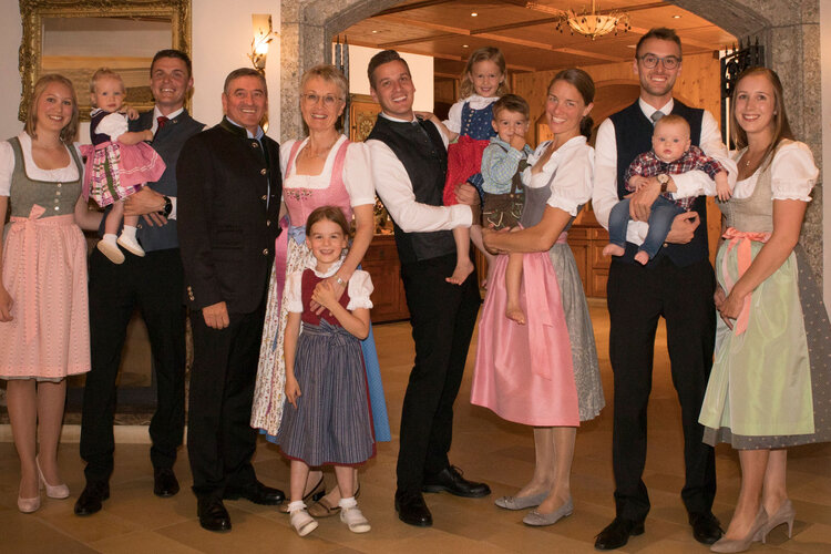 Eine fröhliche Familie posiert in traditioneller Tracht vor einem rustikalen Hintergrund, umgeben von warmem Licht.