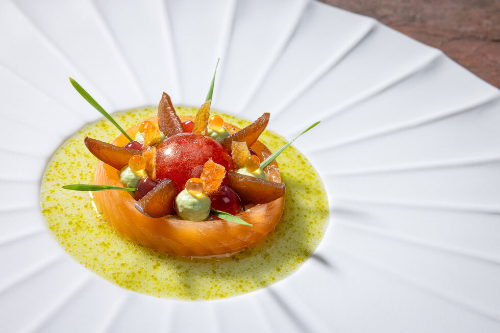 Ein kunstvoll angerichteter Teller mit einer bunten Komposition aus Obst, Gemüse und einer leuchtenden Sauce in der Mitte.
