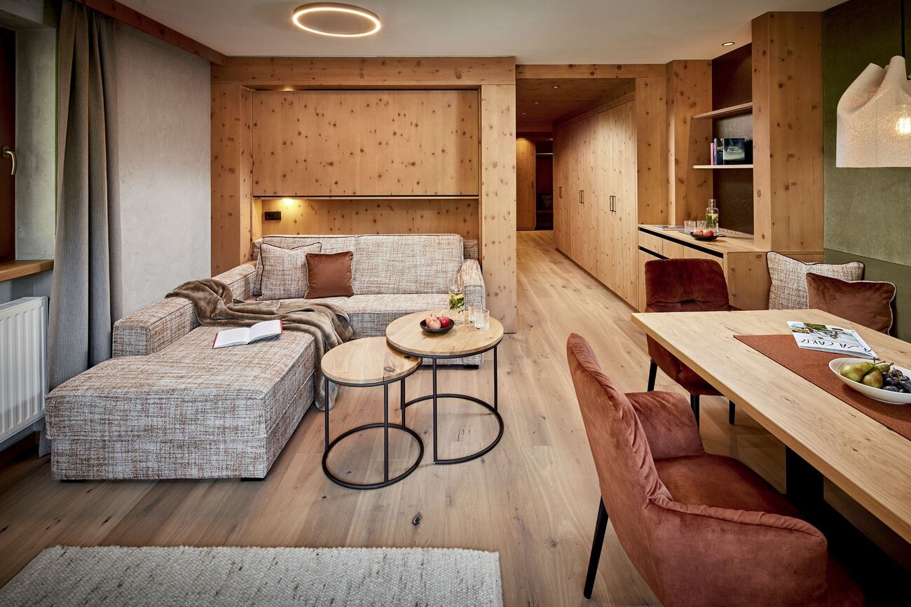 Ein gemütliches Wohnzimmer mit einer beigen Couch, einem kleinen Tisch und warmen Holzelementen, die eine einladende Atmosphäre schaffen.