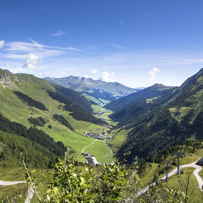 Ein atemberaubender Blick auf das grüne Tal, umgeben von majestätischen Bergen und einem strahlend blauen Himmel.