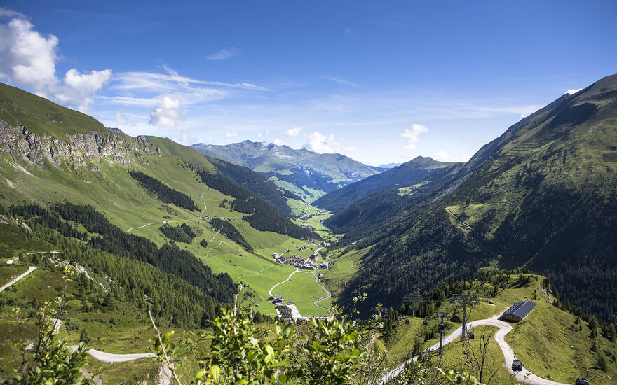 Ein atemberaubender Blick auf das grüne Tal, umgeben von majestätischen Bergen und einem strahlend blauen Himmel.
