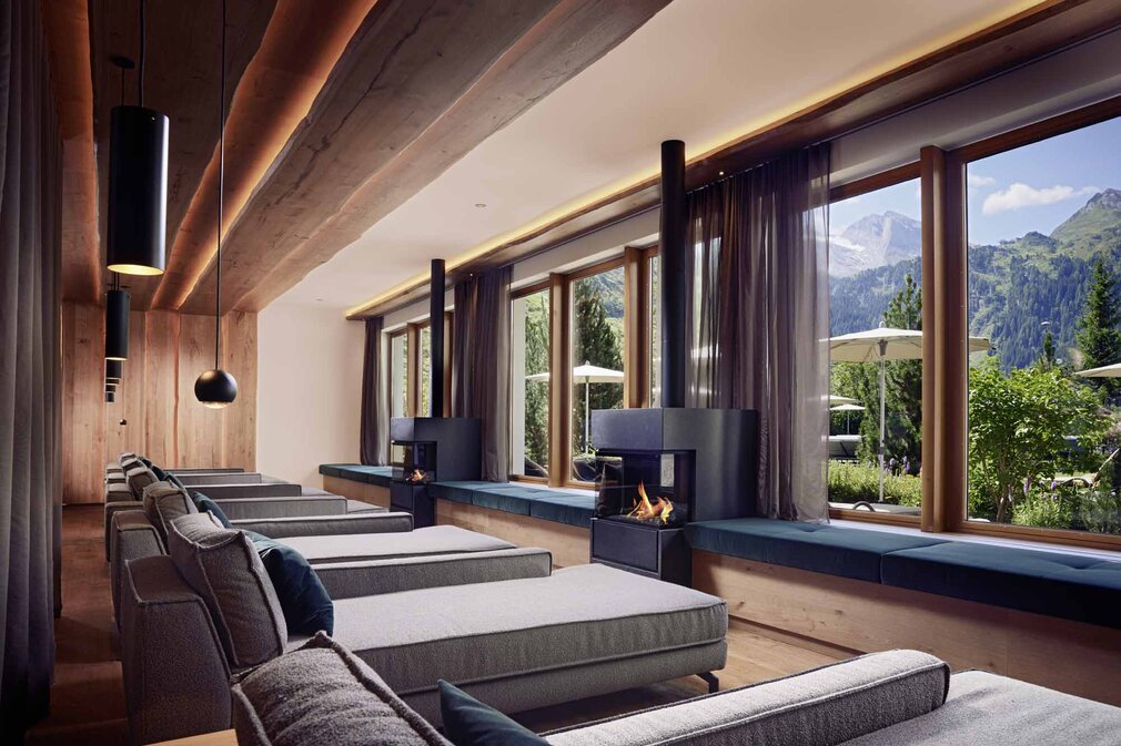 Ein eleganter Ruheraum mit gemütlichen Liegen, großen Fenstern und Blick auf die Berge und die Natur draußen.