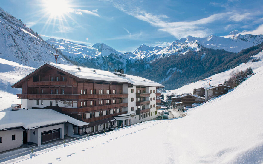 Ein malerisches Hotel in den Alpen, umgeben von schneebedeckten Bergen und strahlend blauem Himmel.