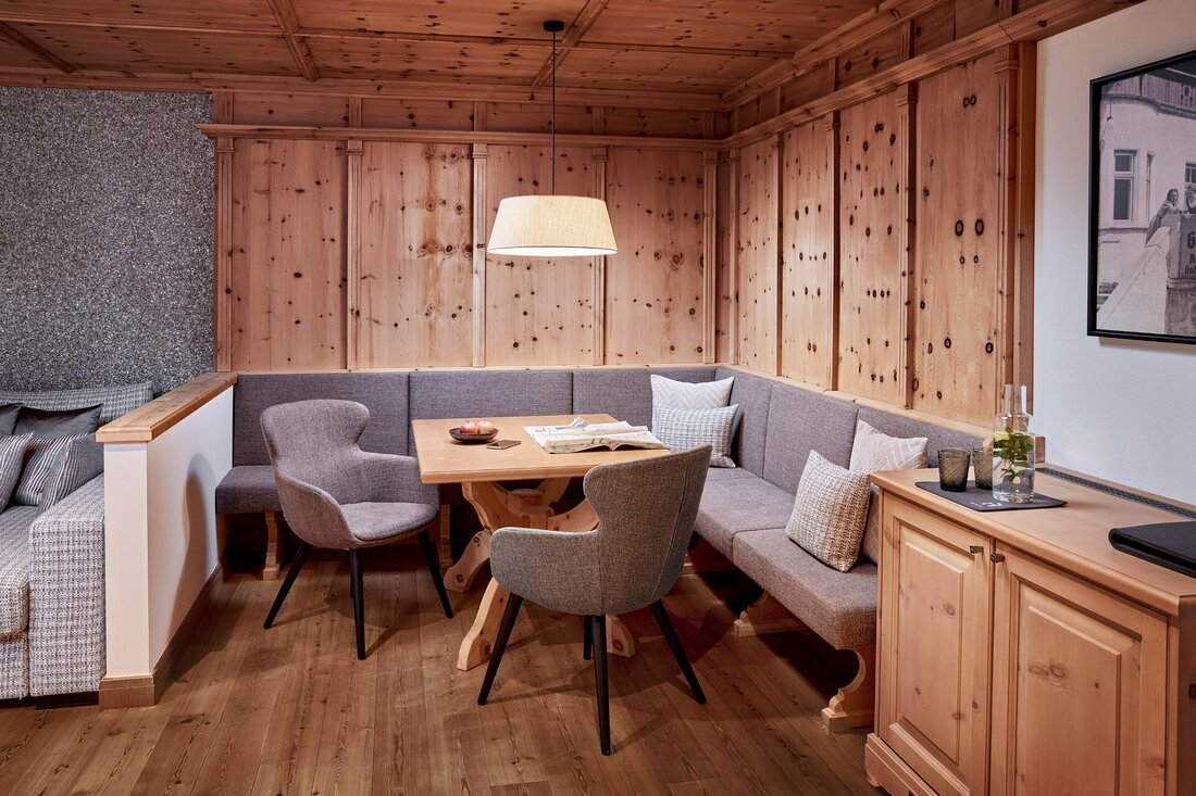 Ein gemütlicher Essbereich mit einer Holzdecke, einer grauen Sitzecke und einem Holztisch, der mit Kerzen dekoriert ist.