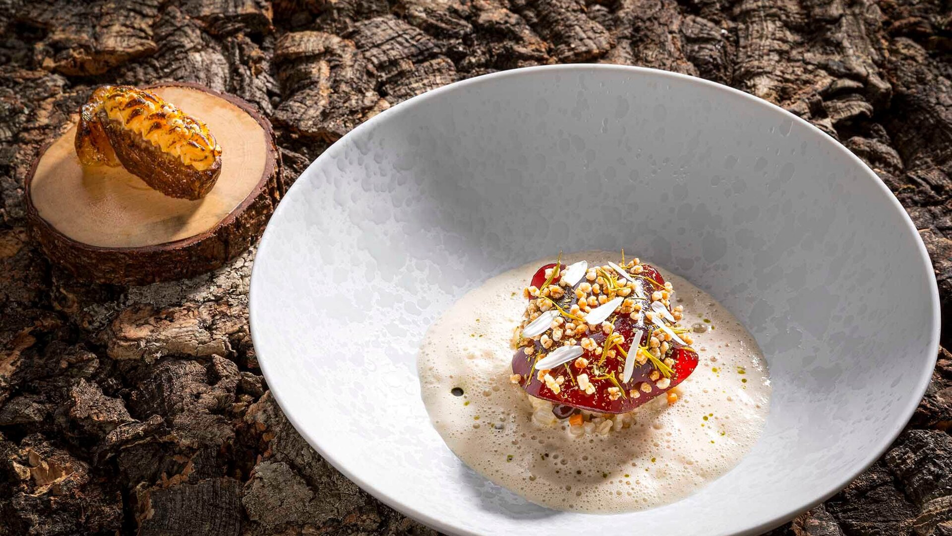 Ein Gourmetgericht präsentiert sich in einer weißen Schüssel, umgeben von einer schaumigen Soße und bunten Toppings.