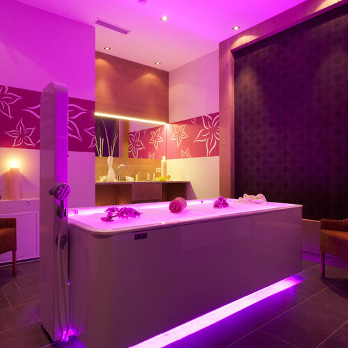 Ein elegantes Spa mit einem modernen Badewanne, umgeben von sanften lila Lichtern und stilvollen Möbeln.