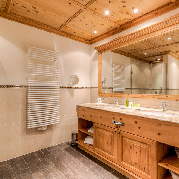 Ein modernes Badezimmer mit Holzdecke, eleganten Waschbecken und einem großen Spiegel, der den Raum reflektiert.