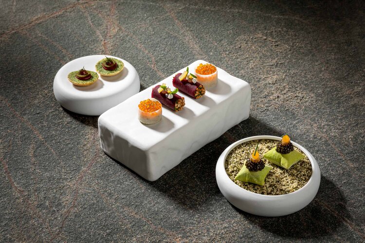 Drei kunstvoll angerichtete Teller mit verschiedenen Delikatessen, darunter Sushi und kreative Häppchen auf einem eleganten Tisch.