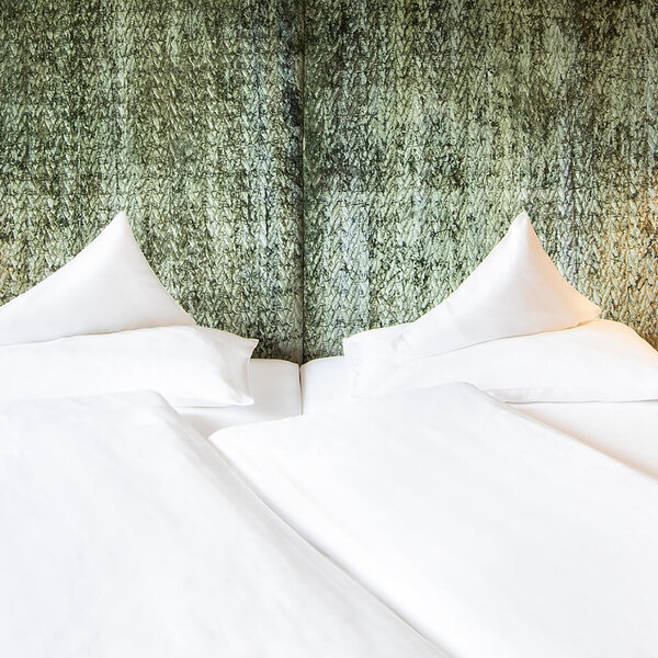 Ein gemütliches Doppelbett mit weißen Bettdecken und Kissen, umgeben von einem eleganten, strukturierten Wandpaneel.