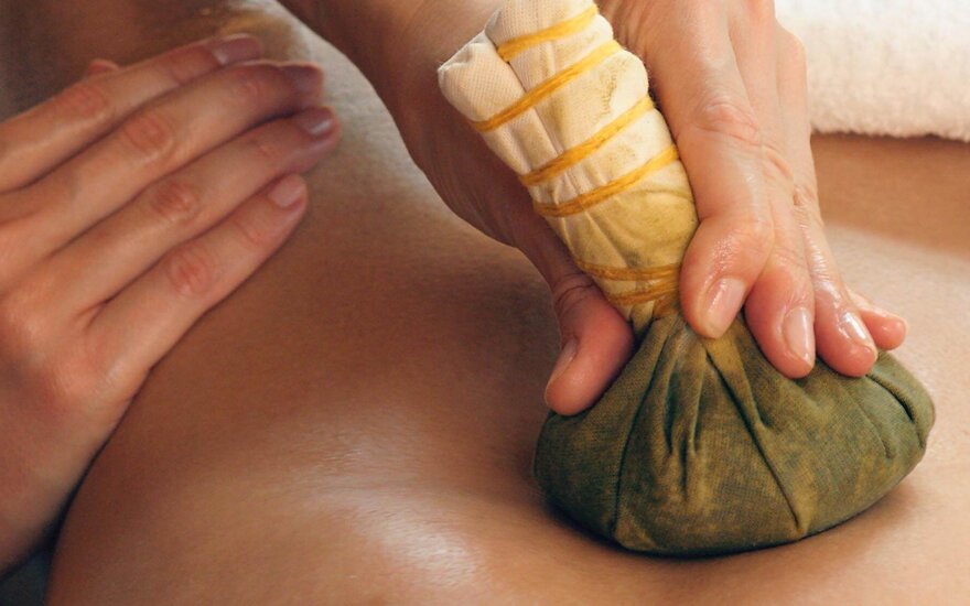 Eine Hand führt eine Stempelmassage mit einem gefüllten Tuchbeutel auf dem Rücken einer Person durch.