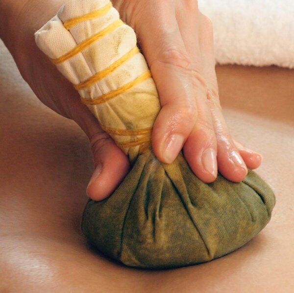 Eine Hand führt eine Stempelmassage mit einem gefüllten Tuchbeutel auf dem Rücken einer Person durch.