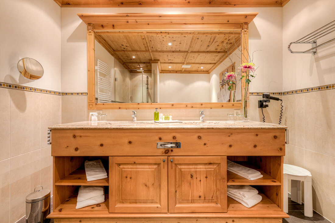 Ein elegantes Badezimmer mit einem Holzwaschtisch, einem großen Spiegel und frischen Blumen auf der Ablage.