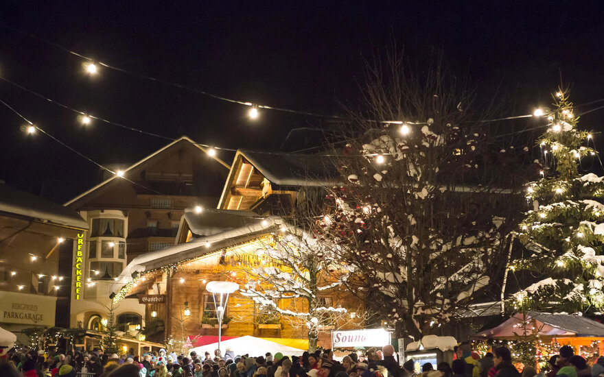 Eine lebhafte Nachtaufnahme eines Weihnachtsmarktes, wo Lichter und Schnee eine magische Atmosphäre schaffen.