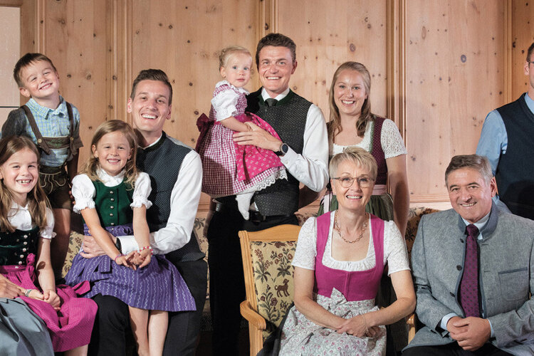 Eine fröhliche Familie posiert in traditioneller Tracht in einem gemütlichen Raum mit Holzverkleidung und einem Sofa.