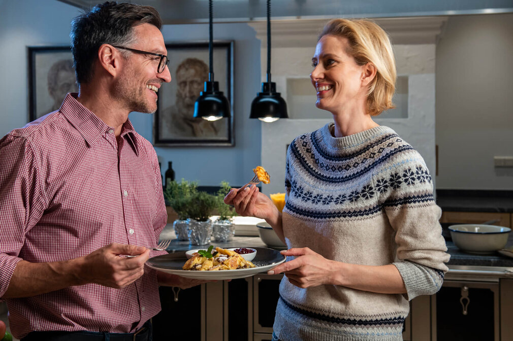 Ein lächelndes Paar genießt ein gemeinsames Essen in einer modernen Küche, während sie sich liebevoll ansehen.