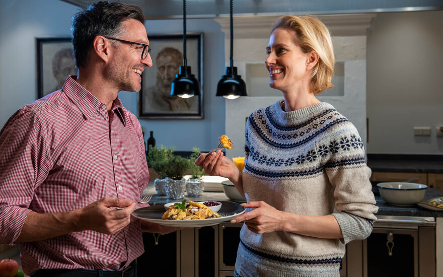 Ein lächelndes Paar genießt ein gemeinsames Essen in einer modernen Küche, während sie sich liebevoll ansehen.
