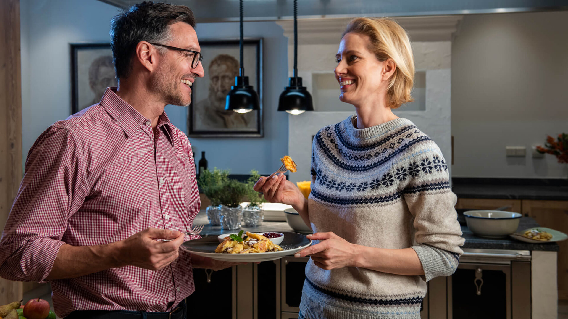 Ein lächelndes Paar genießt ein gemeinsames Essen in einer modernen Küche, während sie sich liebevoll ansehen.