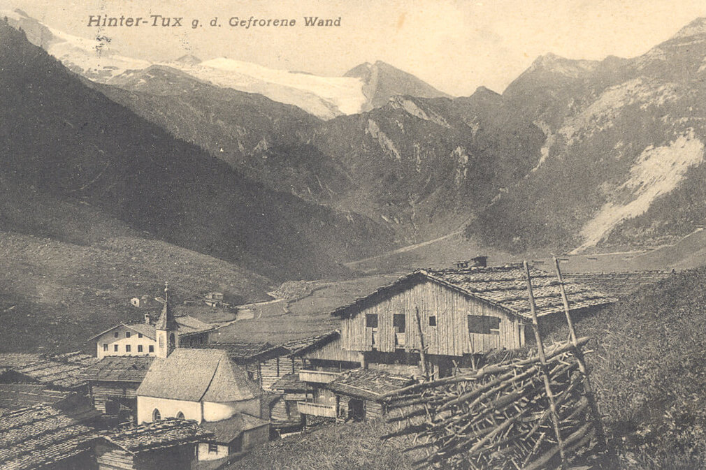 Eine malerische Berglandschaft mit traditionellen Holzhäusern und einer Kirche, umgeben von majestätischen Gipfeln.
