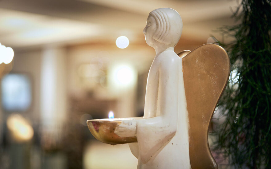 Eine elegante Engelstatue hält eine Schale mit einer brennenden Kerze, umgeben von einem warmen, einladenden Ambiente.