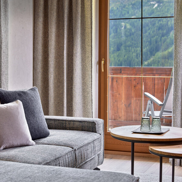 Ein modernes Wohnzimmer mit einem grauen Sofa, dekorativen Kissen und einem Blick auf die Berge durch große Fenster.