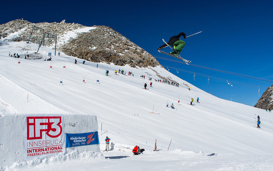 Ein Skifahrer springt über eine Rampe im Hintertuxer Gletscher, während Zuschauer auf der Piste zuschauen.