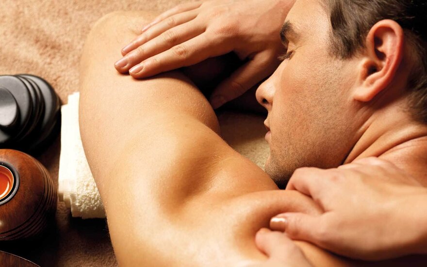 Ein Mann erhält eine entspannende Rückenmassage, während er auf einer weichen Unterlage liegt, umgeben von Wellness-Elementen.