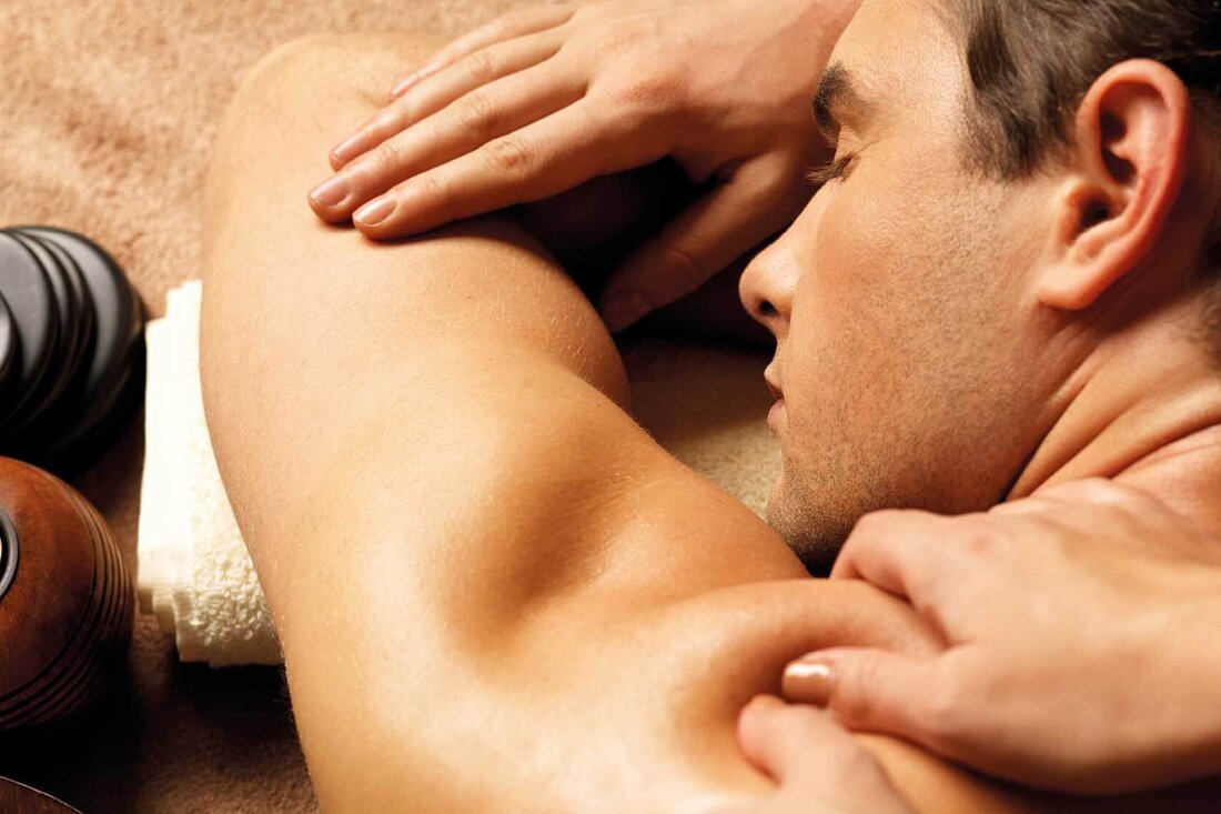 Ein Mann erhält eine entspannende Rückenmassage, während er auf einer weichen Unterlage liegt, umgeben von Wellness-Elementen.