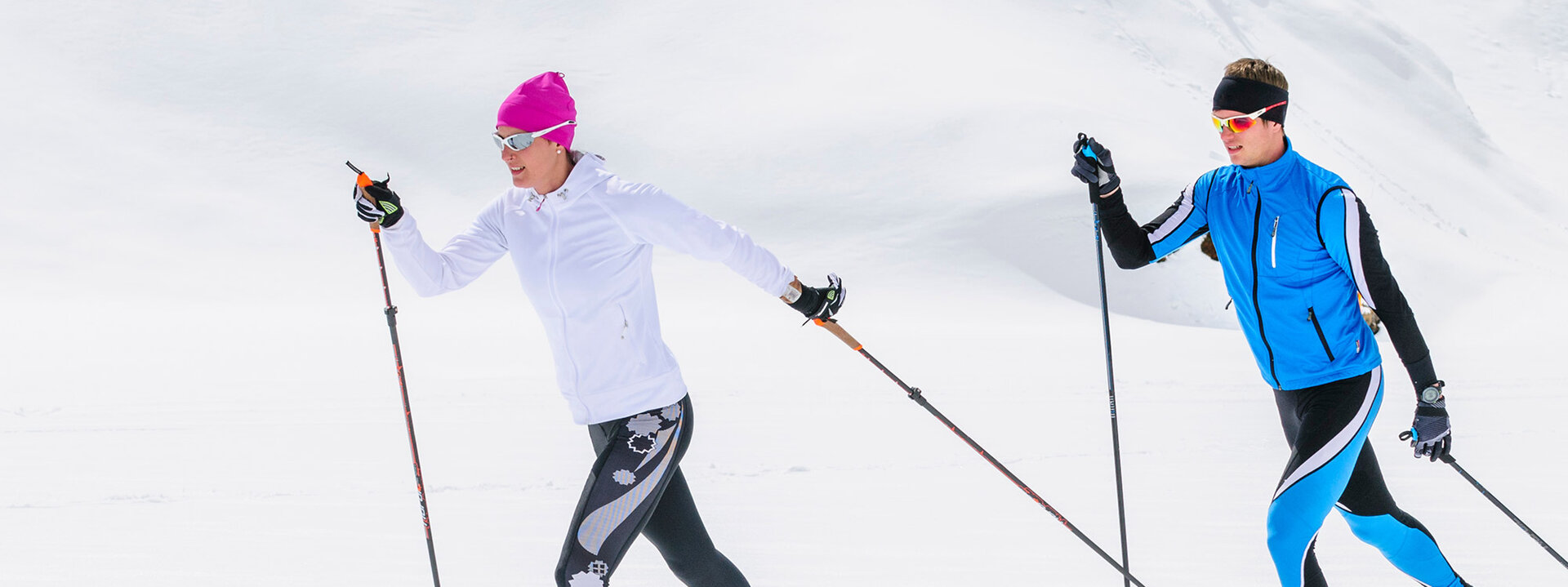 Zwei Skifahrer gleiten über eine schneebedeckte Landschaft, während die Sonne hell am Himmel scheint.